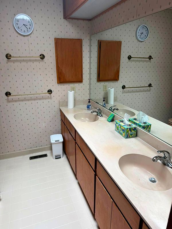 Before: dated double vanity, wallpaper and small square floor tile