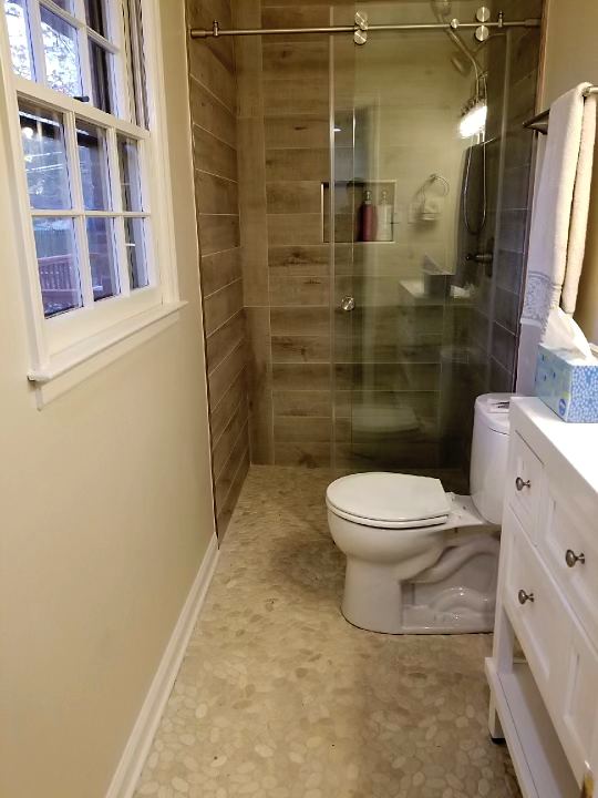 After: curbless walk-in shower with a glass panel and pebble tile floor